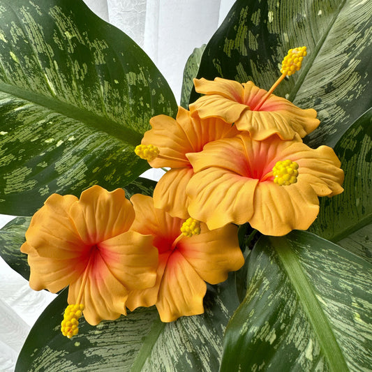 5 palm-sized artificial foam hibiscus flowers that are orange with pink centres, and with green foliage in the background